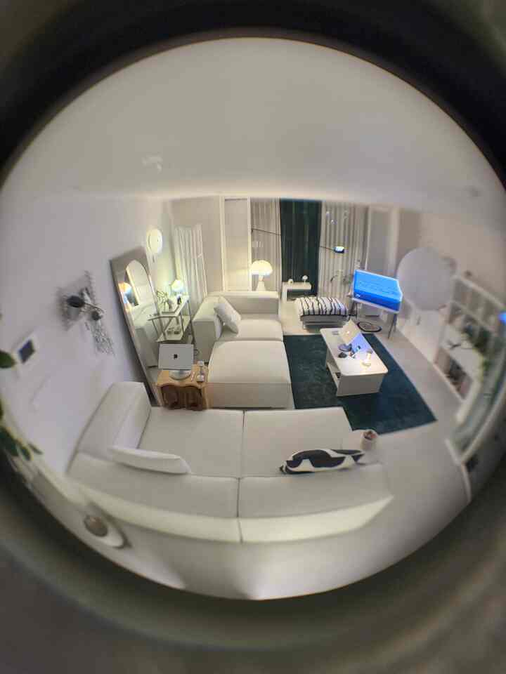 白を基調としたリビング、大きなセクショナルソファと複数の照明、ラグ、ノートパソコンが配置されたモダンで清潔感のある空間