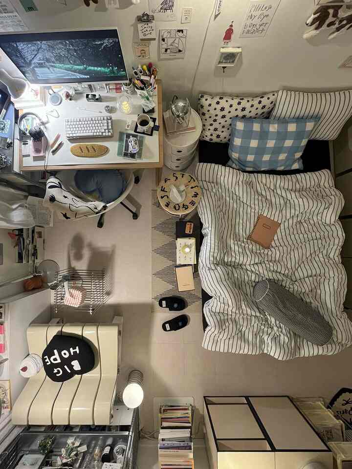 白を基調とした小さな寝室、デスクとクッションのあるベッドが配置されたシンプルなホームオフィス空間