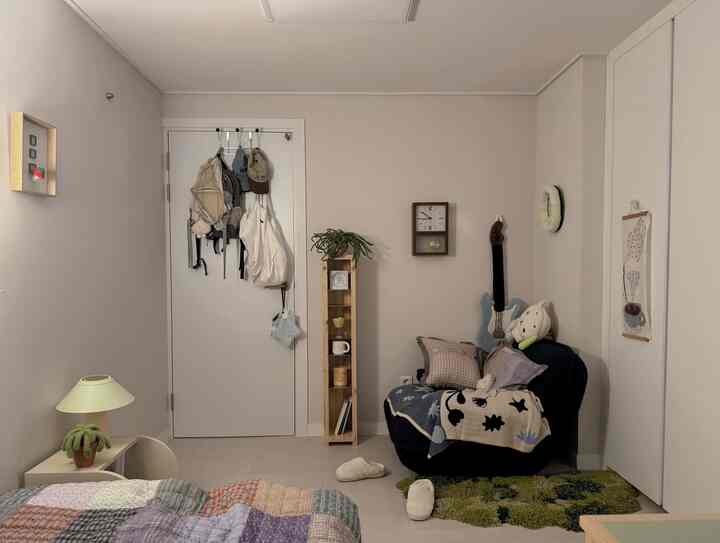 Beige and wood tone studio bedroom featuring dark blue sofa with patterned throw, rug, and charming small decor items creating cozy atmosphere