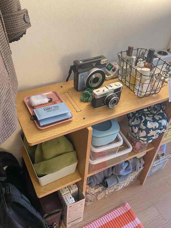 ナチュラルな色調のワンルーム、木製のモジュラーシェルフと多様なバスケットが配置されたコンパクトで整理されたインテリア