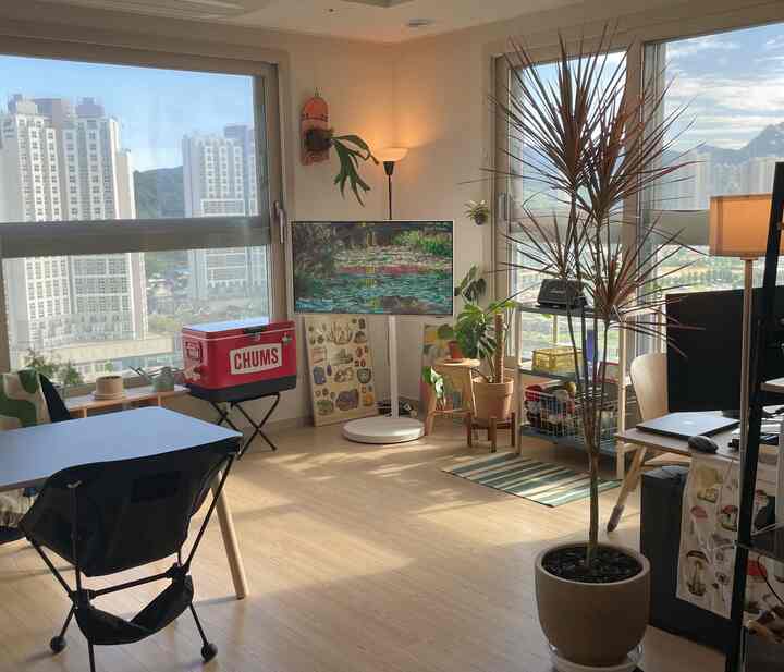 明るい木目調の床と白い壁が調和する二人暮らしのリビングルーム、ダイニングテーブルとキャンプチェア、多彩な植物が配置されたナチュラルモダンなインテリア