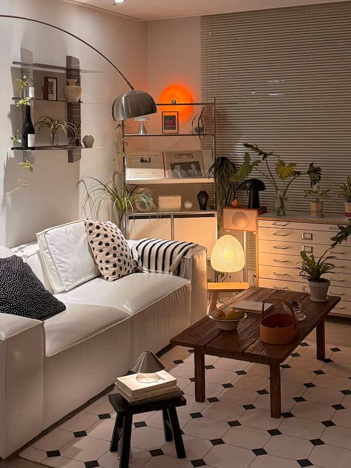 Warm brown and white toned living room with large sofa, wooden coffee table, plants, and ambient lighting creating a cozy atmosphere