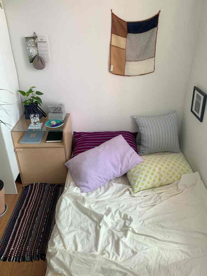 ナチュラルな色調の小さな寝室、白い寝具とカラフルな枕、シンプルな木製サイドテーブルが配置された落ち着いたインテリア