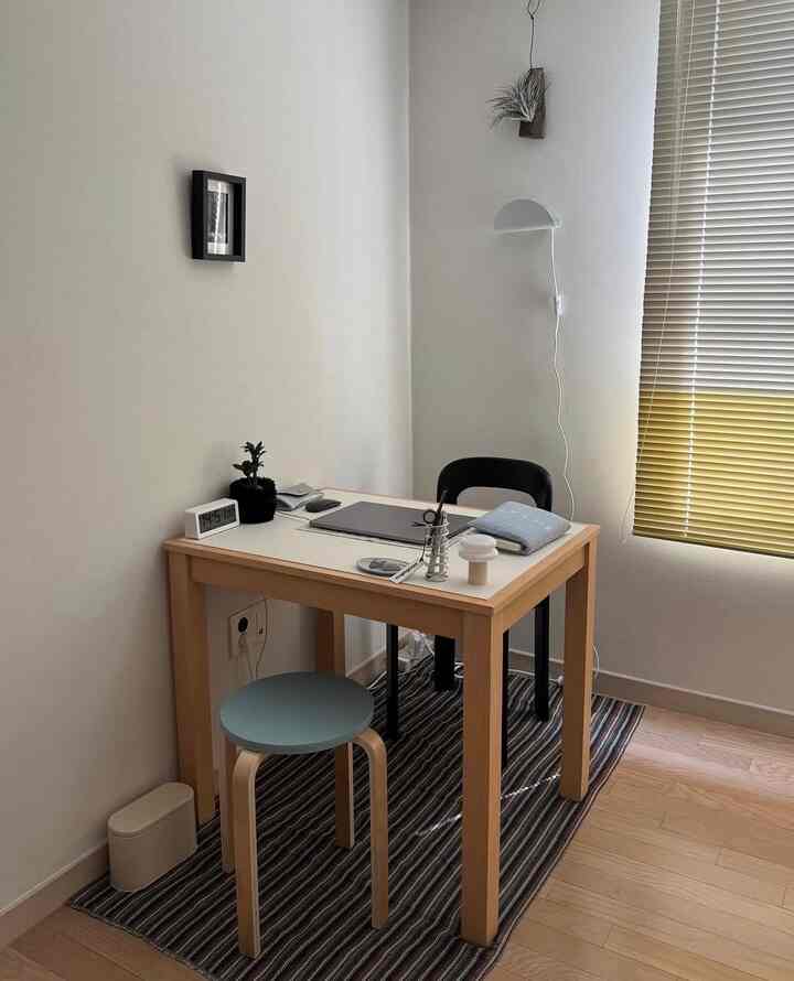 ナチュラルな木調とモダンスタイルのコンパクトな部屋、デスクとスツール、ブラインドが配置されたすっきりとした作業空間