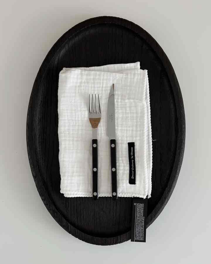 黒のトレイの上に白いキッチンタオルと黒い持ち手のカトラリーが整然と配置されたシンプルなキッチン用品の写真