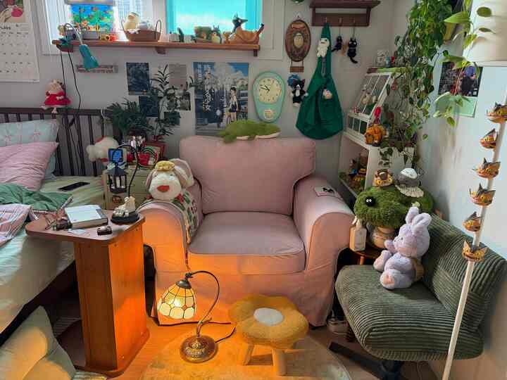 ピンクのアームチェアとグリーンの椅子が置かれたコンパクトなリビング、植物とヴィンテージの壁時計が雰囲気ある空間を演出