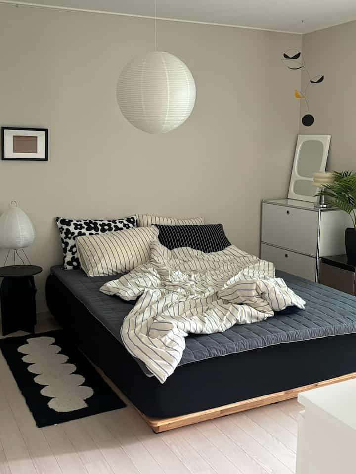 白と黒のトーンの寝室、ストライプ柄の寝具とモダンな家具が配置された印象的な空間