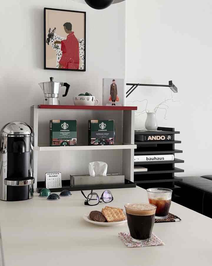 白い壁とミニマルな黒いソファ、コーヒーマシンとカップが並ぶテーブルのあるおうちカフェ空間