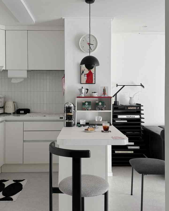 モノトーンのキッチン空間、白いダイニングテーブルと黒い椅子、ペンダントライトと時計が配置された印象的なインテリア