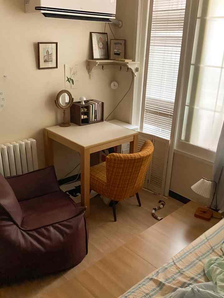 ナチュラルな色調の寝室兼ホームオフィス空間、木製デスクとアームチェア、ビーンバッグソファが配置された落ち着いた雰囲気の部屋