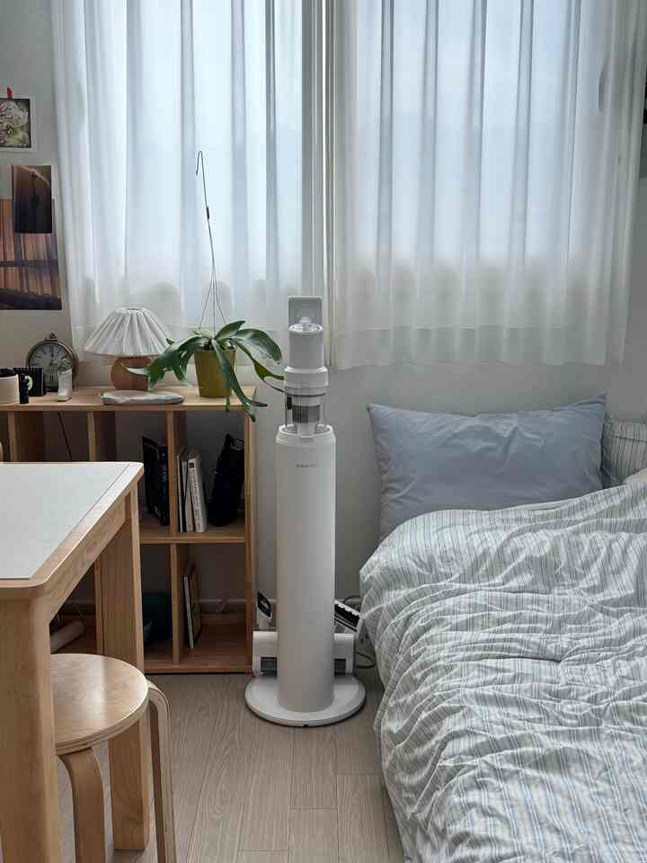 ナチュラルな色調のコンパクトな寝室、シンプルな家具と白い掃除機が配置された落ち着いた空間