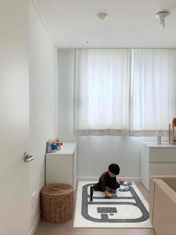 白とナチュラルカラーの子供部屋、道路模様のラグと収納チェスト、子供がおもちゃで遊ぶ雰囲気のある空間