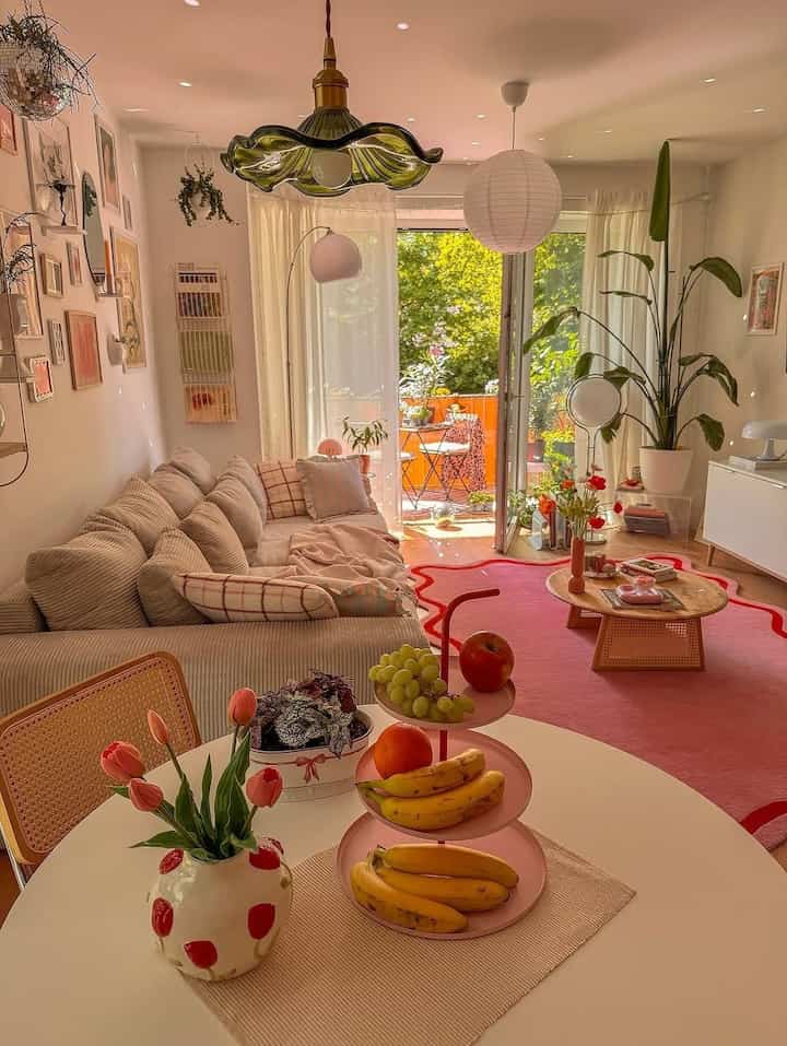 Bright natural-toned living room with balcony, striped sofa and pink rug creating a cozy atmosphere