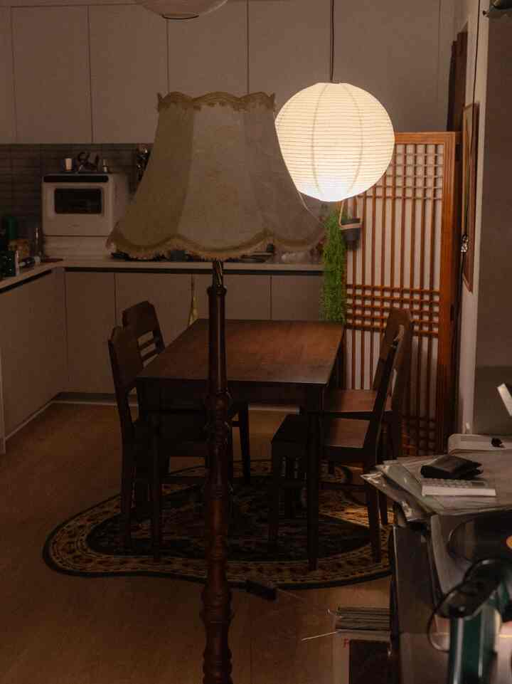 ナチュラルカラーのダイニングルーム、木製のダイニングテーブルと椅子、ヴィンテージのフロアランプとペンダント照明が配置された雰囲気のある空間