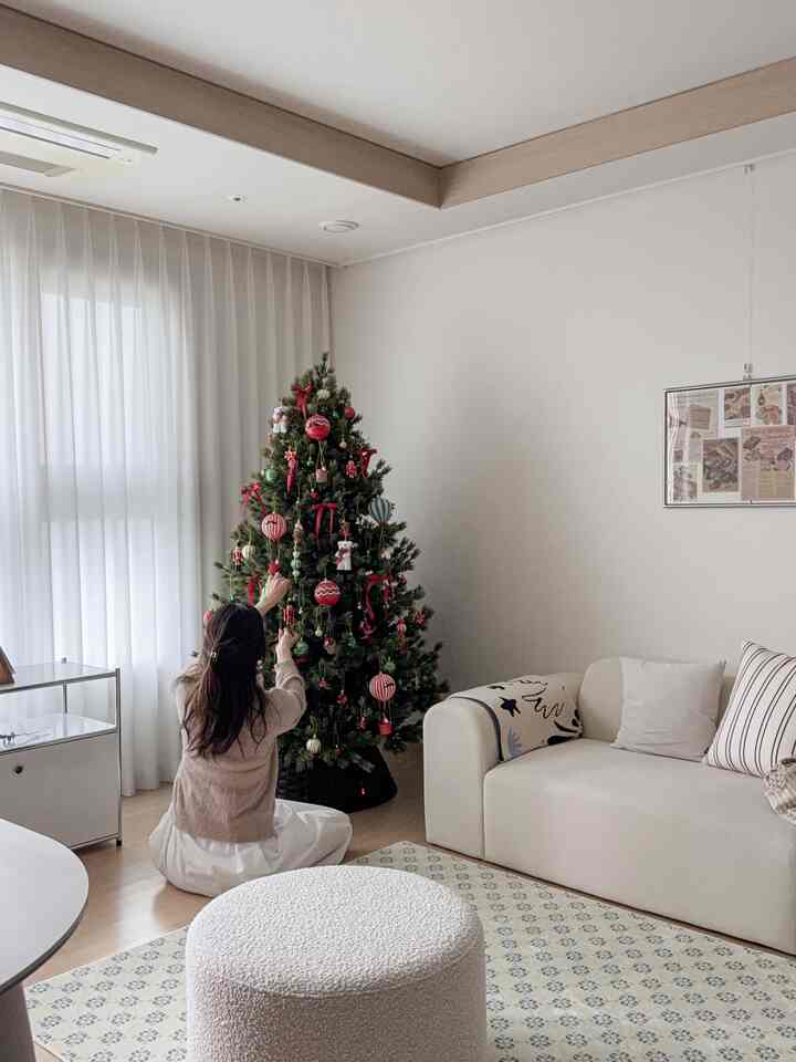 White and natural toned living room featuring a 180cm large Christmas tree, round stool, and sofa creating a cozy winter atmosphere