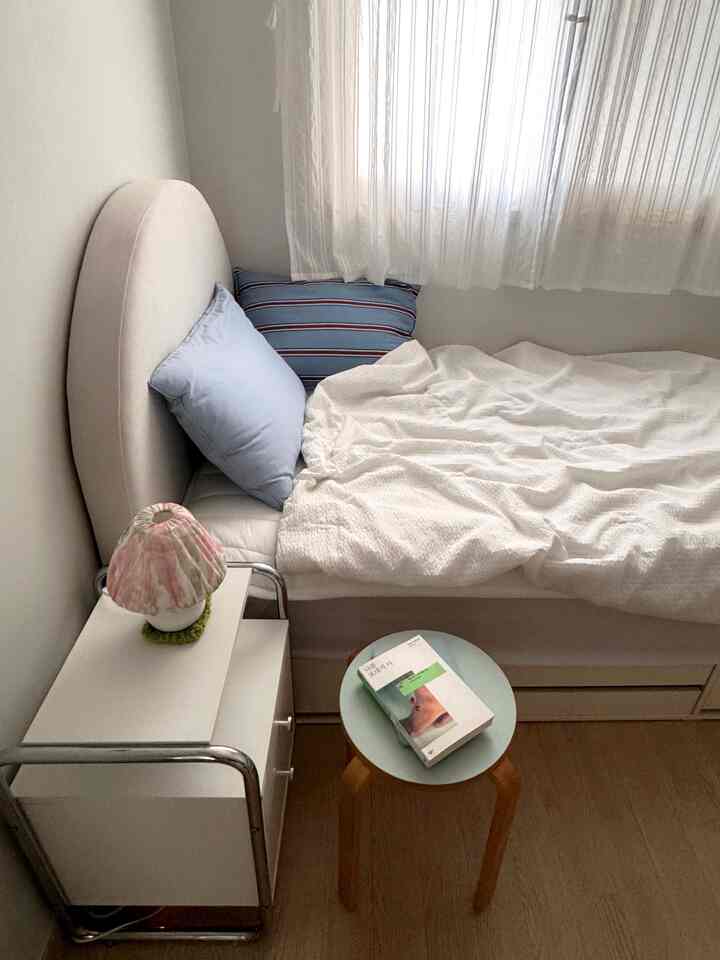 白い壁とベッドがある6畳の一人暮らし向け寝室、ナイトテーブルと枕が配置された落ち着いた空間