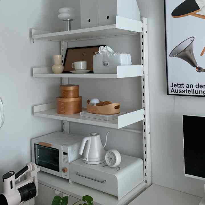 白いトーンのワンルームキッチンスペース、壁の無打孔棚に電気ケトルやミニオーブンなどのキッチン用品が整然と配置されたミニマルなインテリア