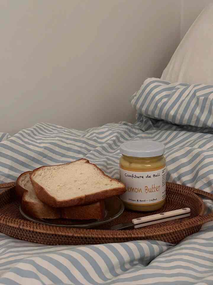 白と青のストライプの寝具の上にラタンのトレーが置かれ、パンとレモンバターの瓶がある雰囲気のある寝室のインテリア