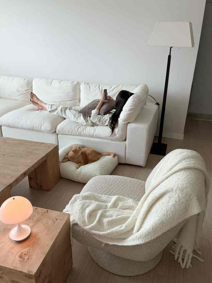 アイボリーと木目調のリビング、大きなソファとアームチェア、猫用クッションが配置された雰囲気のある空間