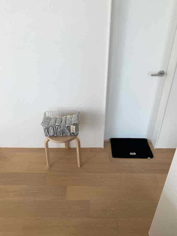 白い壁と木目調の床、スツールの上にステンレス製ワイヤーバスケットが置かれたすっきりとした玄関の空間