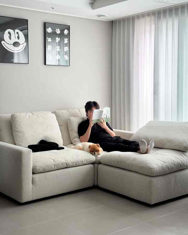 ベージュとホワイトのトーンのリビングルーム、広いファブリックソファと白いカーテンが配された落ち着いたモダンなインテリア