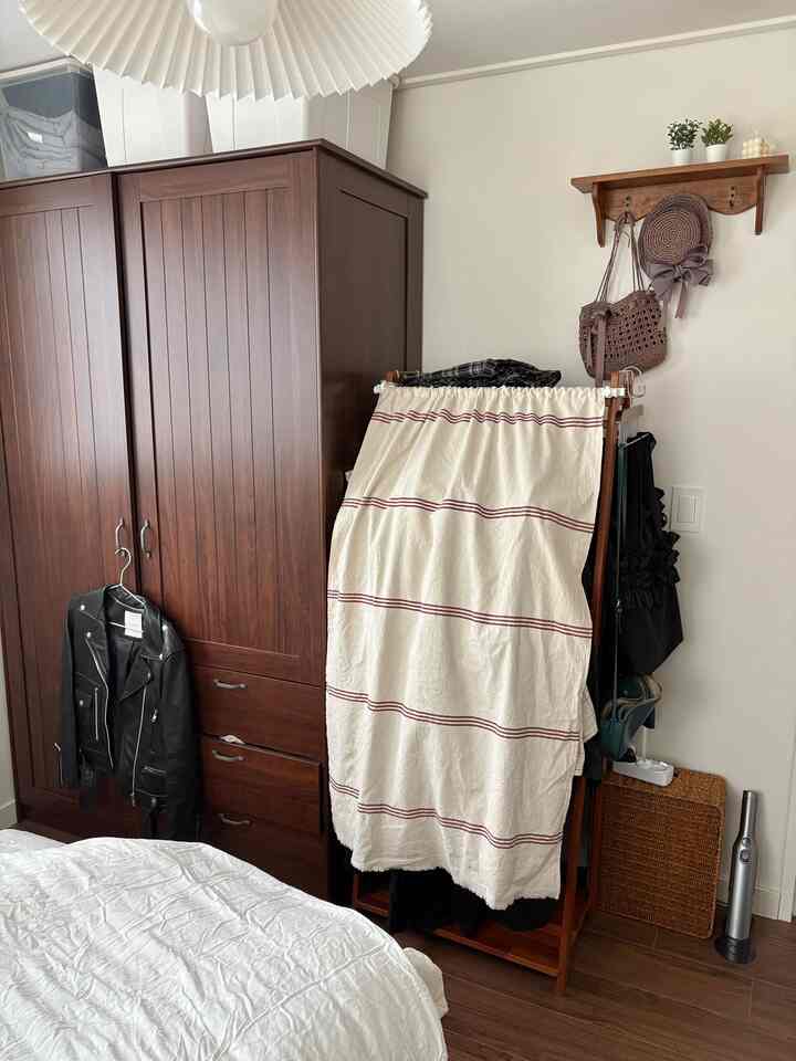 ブラウンとホワイトのトーンの寝室、ダークなワードローブと洋服ラック、白い寝具が配置された落ち着いた空間