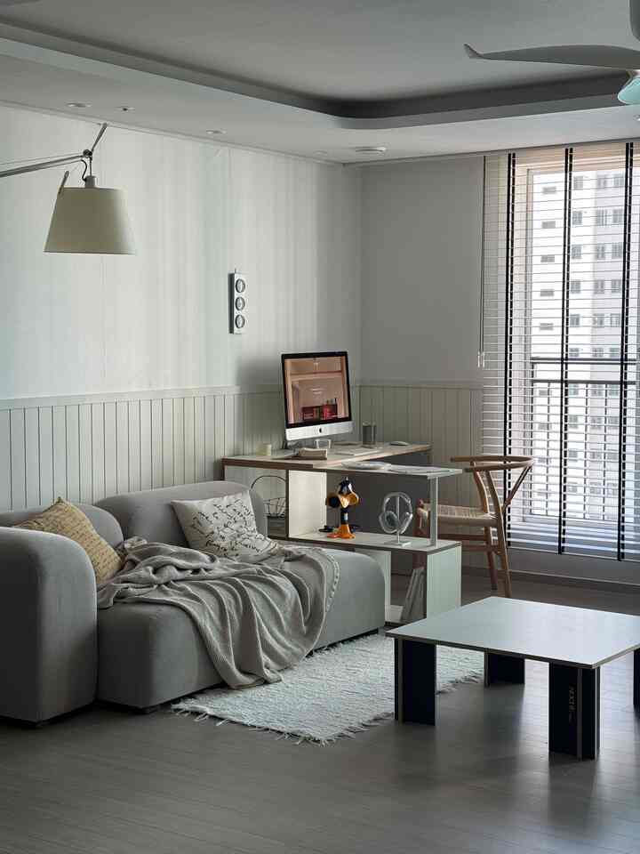 A modern and calm living room in white and gray tones featuring a sofa and a desk with a computer