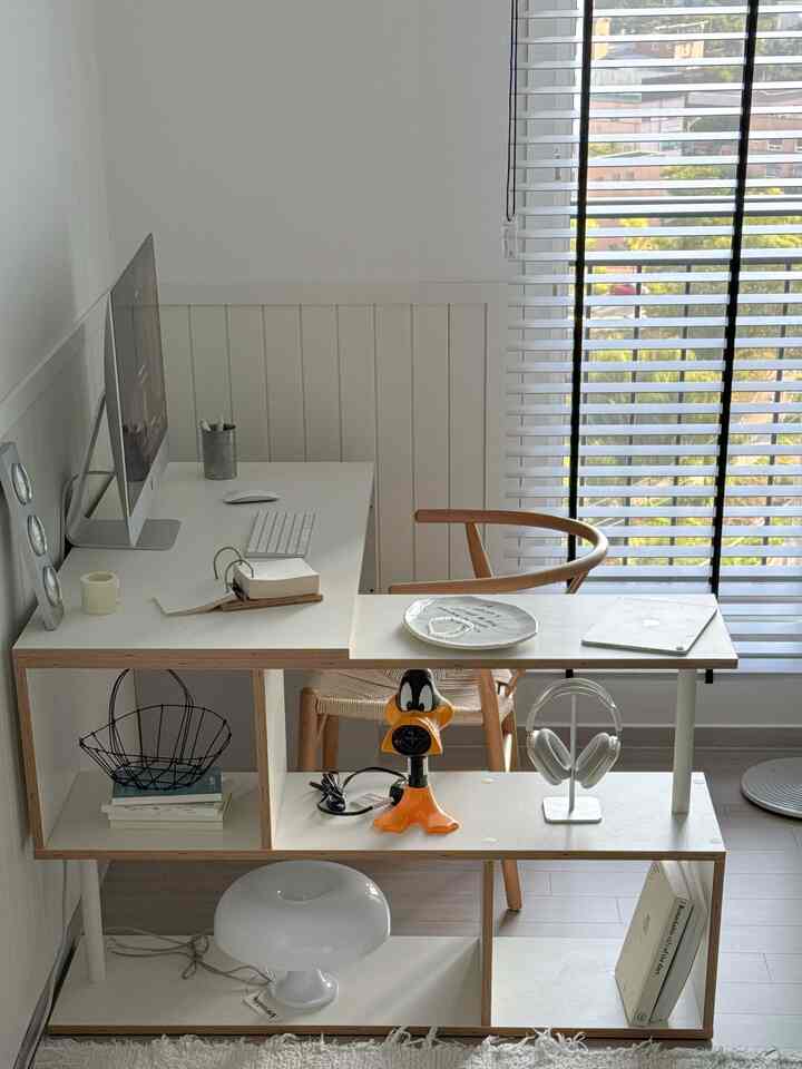 White and natural tone home office with a white desk, monitor, and shelves displaying objets in a neat arrangement