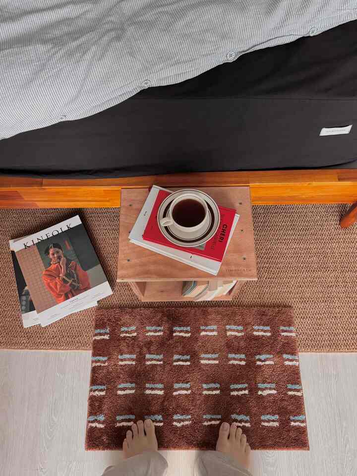 ブラウンとナチュラルカラーの寝室空間、ベッド横のナイトテーブルに本とお茶のカップが置かれた雰囲気のあるインテリア