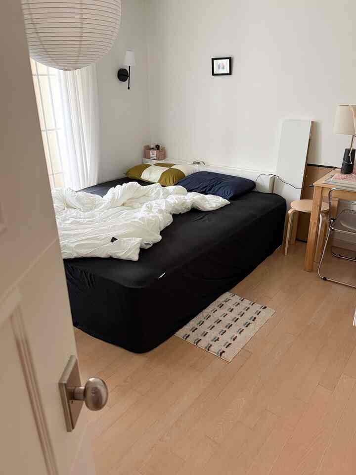 白い壁とナチュラルウッドの床がある寝室、黒いベッドとシンプルな家具が配置された雰囲気のあるインテリア