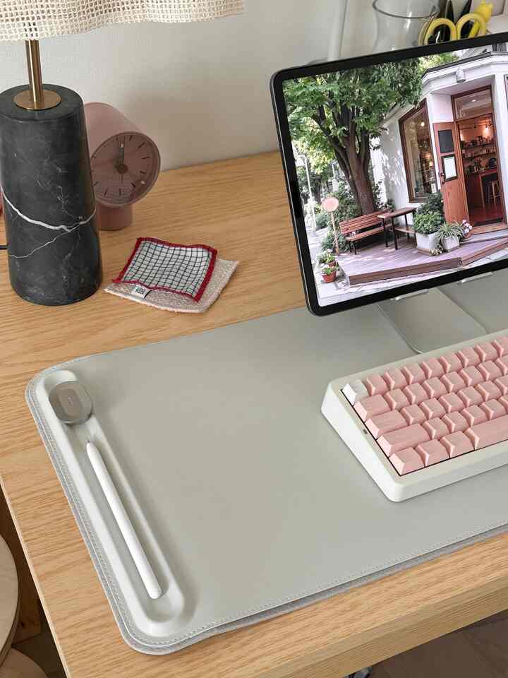 木目調のデスクにピンクのキーボードとグレーのデスクマットが置かれた、整ったホームオフィスのインテリア