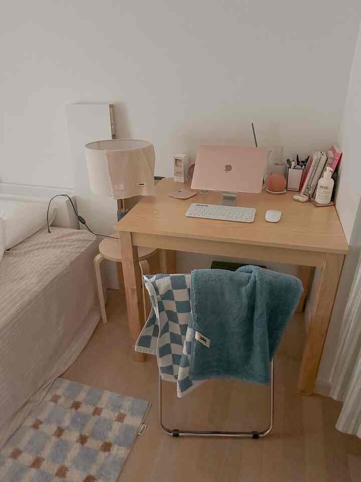 ナチュラルな木目調の落ち着いた寝室、ホームオフィススペースにパウダーブルーのタオルと整頓されたデスクが配置された雰囲気のあるインテリア