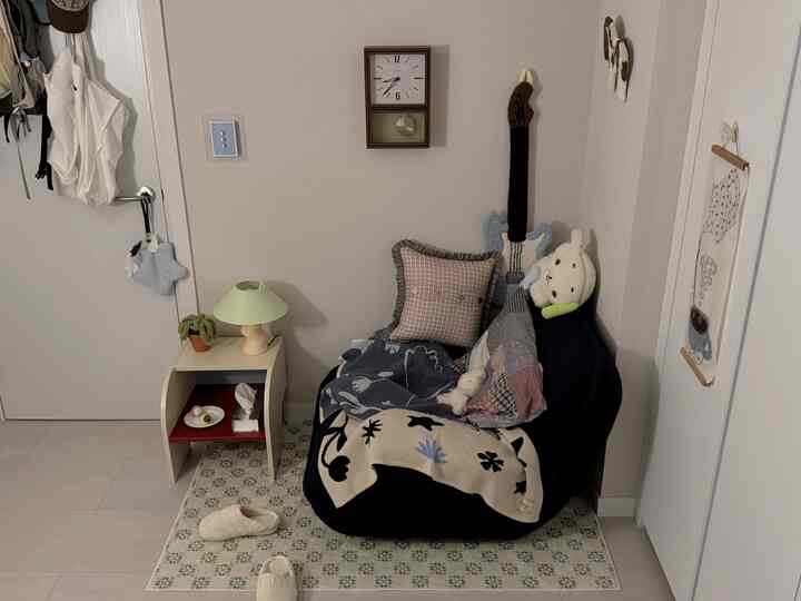 明るいホワイトトーンのコンパクトな寝室のコーナー、ネイビーのアームチェアとアイボリーのナイトテーブルが配置された印象的な空間