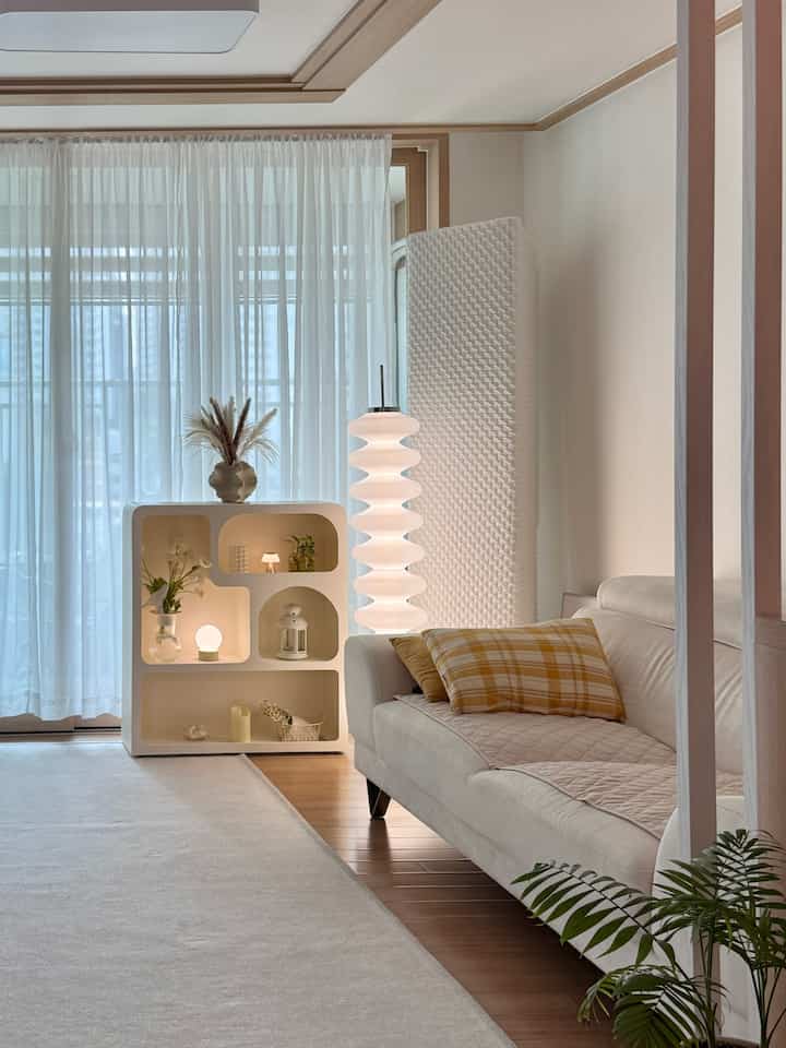 白とベージュの色調のリビング、ソファとフロアランプが配置されたシンプルでナチュラルな雰囲気のインテリア