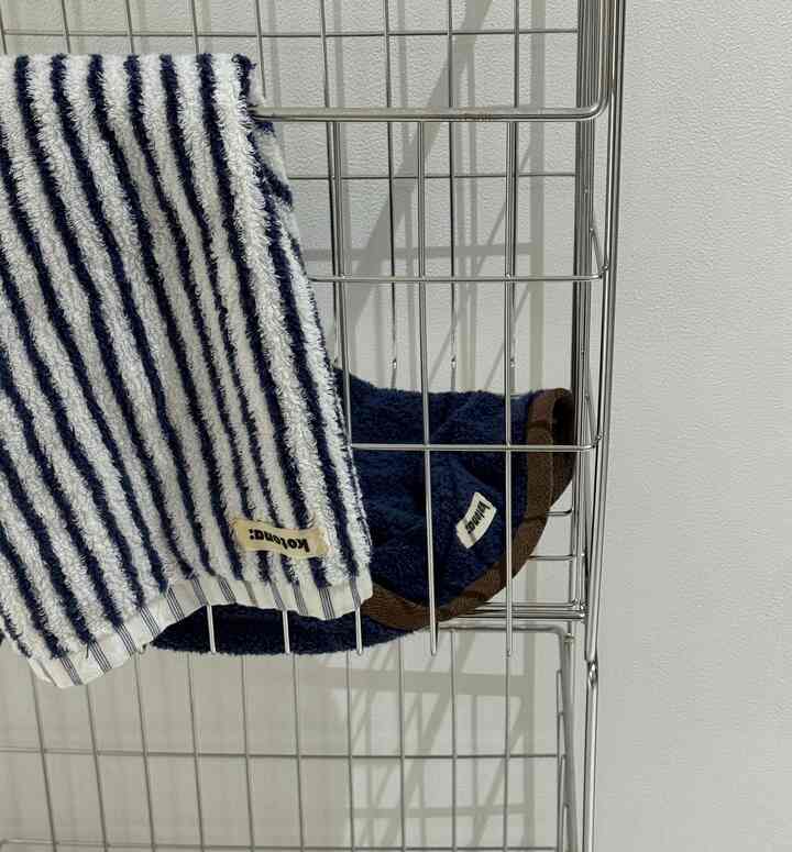 シルバーの金属製タオル掛けにネイビーとストライプのタオルが掛けられた、清潔感のあるバスルームの小物