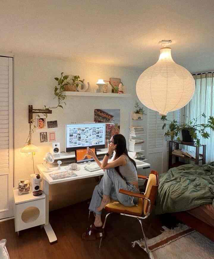 白と木目調が調和した一人暮らしのコンパクトな寝室兼ホームオフィス、黄色のアームチェアと緑のベッドカバーが配置された温かみのあるインテリア