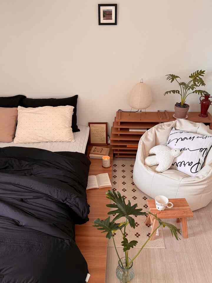 アイボリーとウッドトーン、ブラックが調和する寝室、低いベッドやビーンバッグソファ、照明や植物が配置された居心地の良い空間