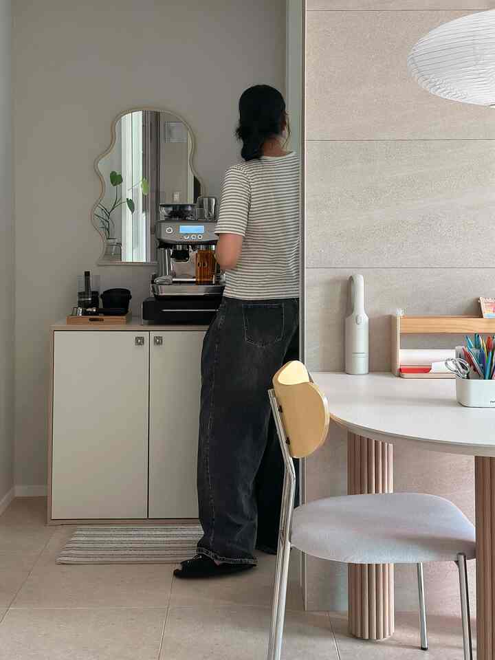 ホワイトトーンのキッチン空間、エスプレッソマシンと不規則形の鏡が配置された雰囲気のあるミニホームカフェ