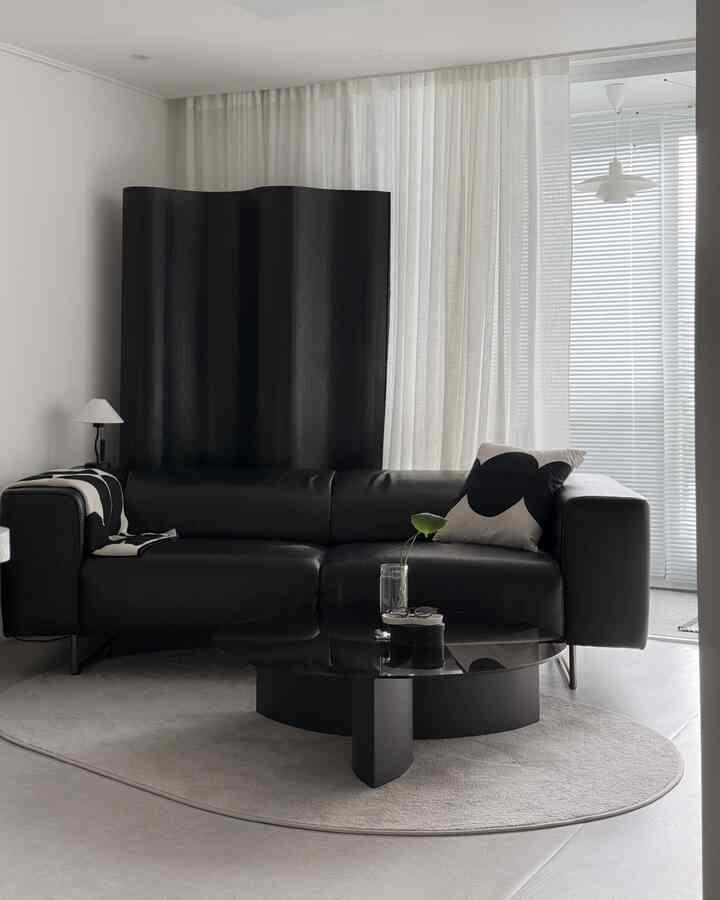 白と黒のトーンのモダンなリビングルーム、黒いレザーソファと透明なガラスのコーヒーテーブルが配置された空間
