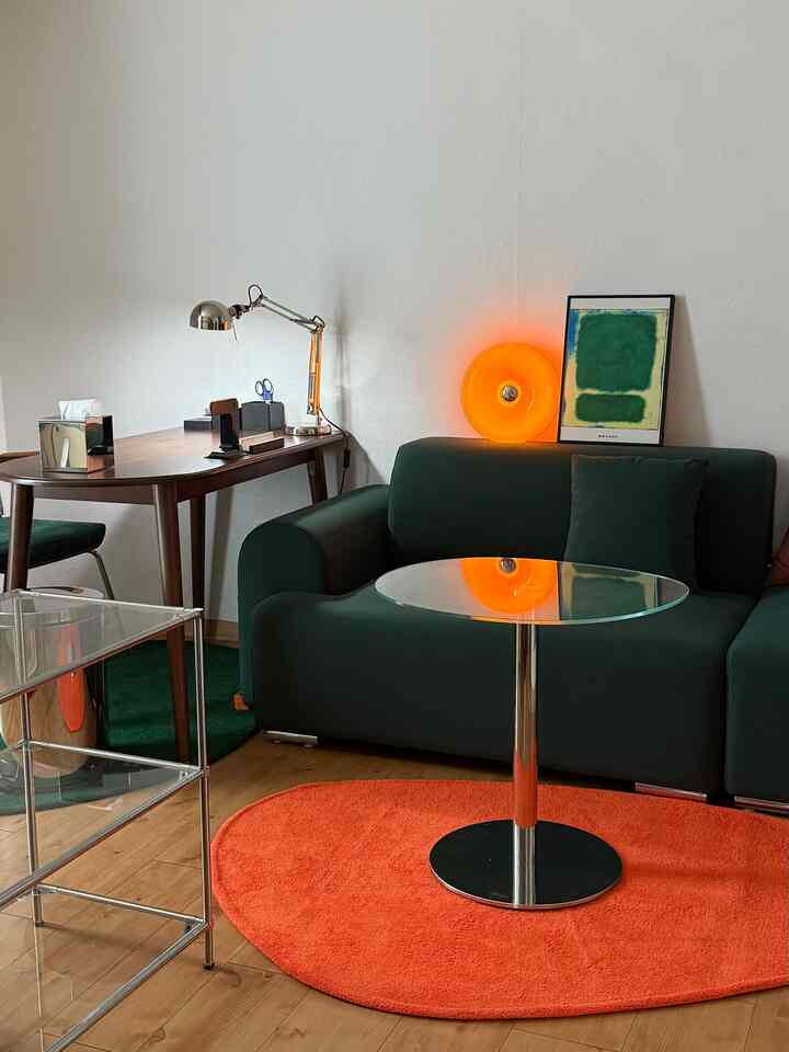 木目調の床と緑のソファがある3坪のワンルームワークスペース、オレンジのラグとミッドセンチュリーモダン家具が調和した印象的な空間