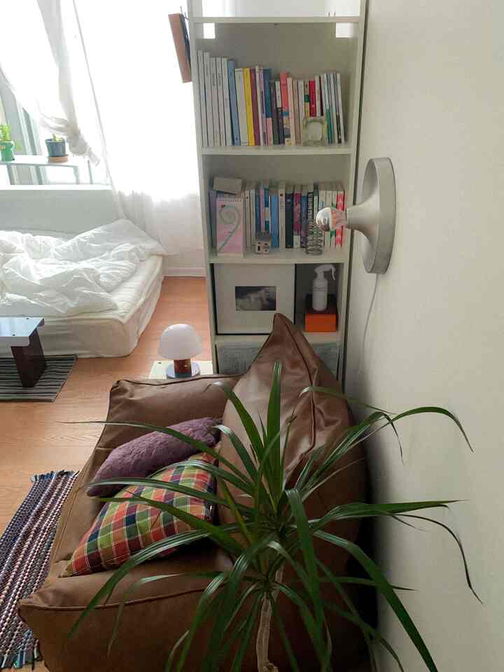 白と茶色のトーンの小さな寝室、ビーズクッションソファと本棚が配置されたナチュラルモダンなインテリア