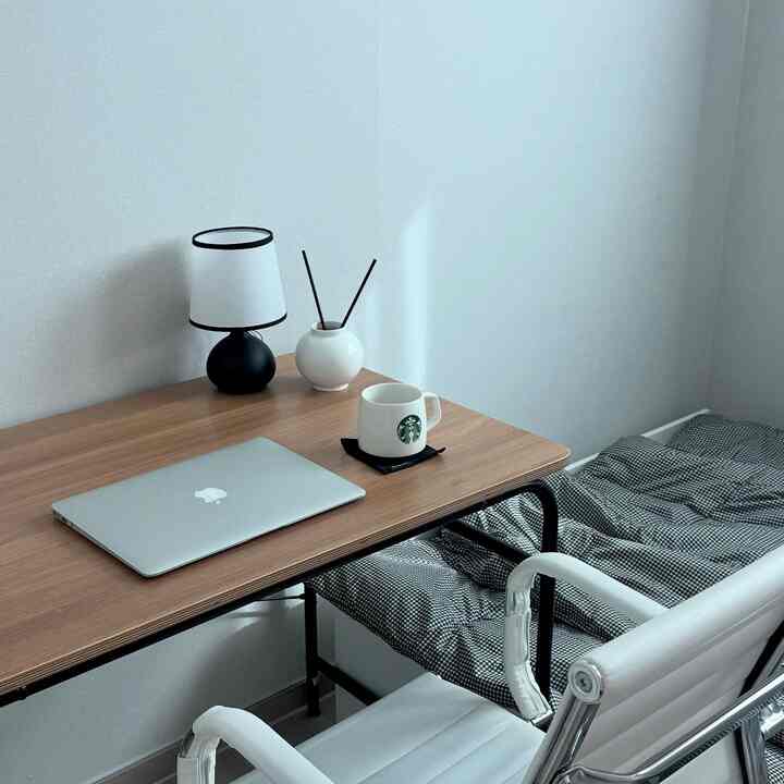 自然な木目調の寝室兼ホームオフィス空間、デスクにノートパソコンとディフューザー、チャコールのチェック柄ベッドカバーが配置された落ち着いたインテリア