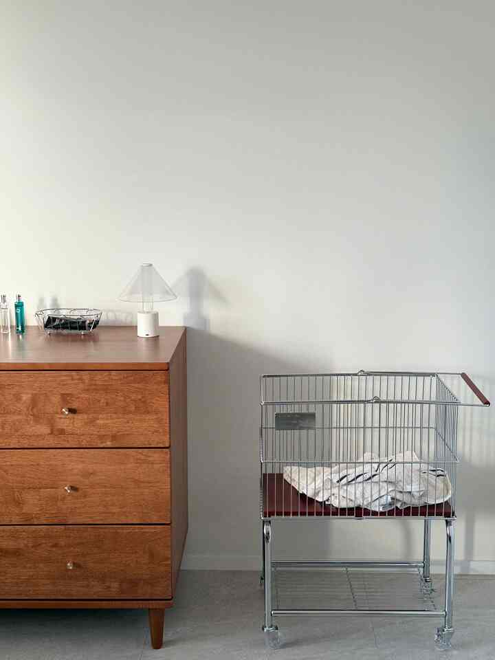 ナチュラルな雰囲気のトイレ入口に置かれた木製のドレッサーとタオルが入ったメタルトロリー、整然とした実用的な収納スペースが印象的なインテリア