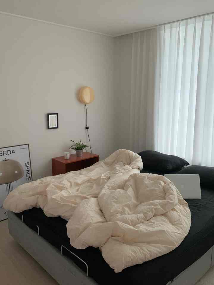 白い壁とカーテン、ベージュの寝具が配置されたモダンな寝室の雰囲気のあるインテリア