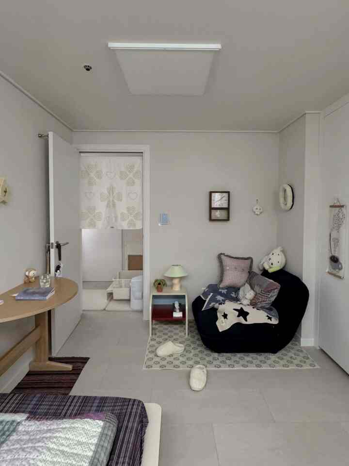 ナチュラルなアイボリートーンのコンパクトなリビング、ビーズクッションソファと小さなナイトテーブル、ラグが配置された落ち着いた空間