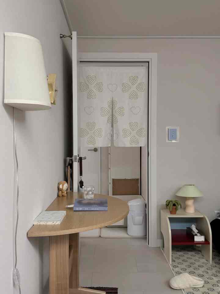 ベージュとホワイトの色調のワンルーム小部屋、半円形の木製テーブルと仕切りカーテンが配置された印象的な空間