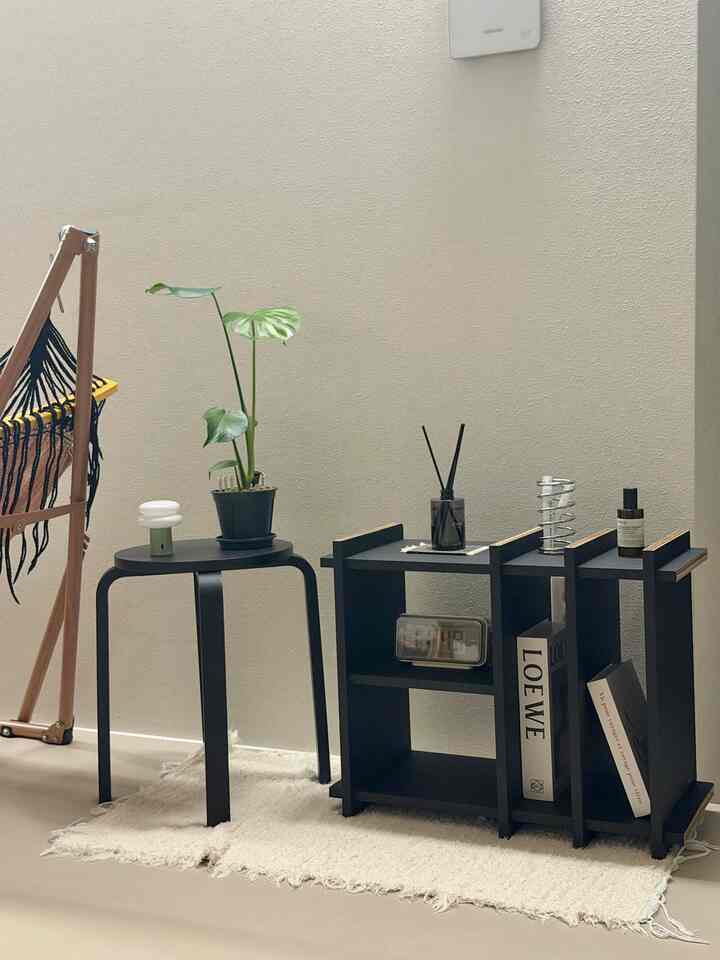 落ち着いた黒を基調としたリビング、黒のスツールと棚に植物やオブジェが配置されたシンプルでモダンなインテリア