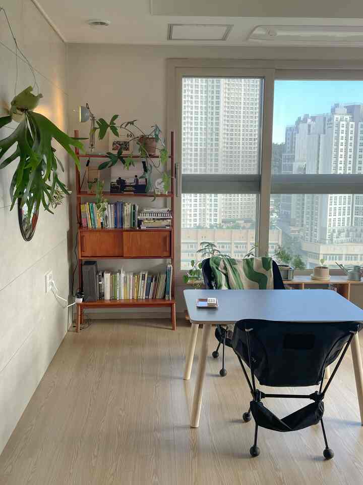 ブラウンの木目調フローリングと本棚があるナチュラルモダンなリビング、窓から都市の景色が見える