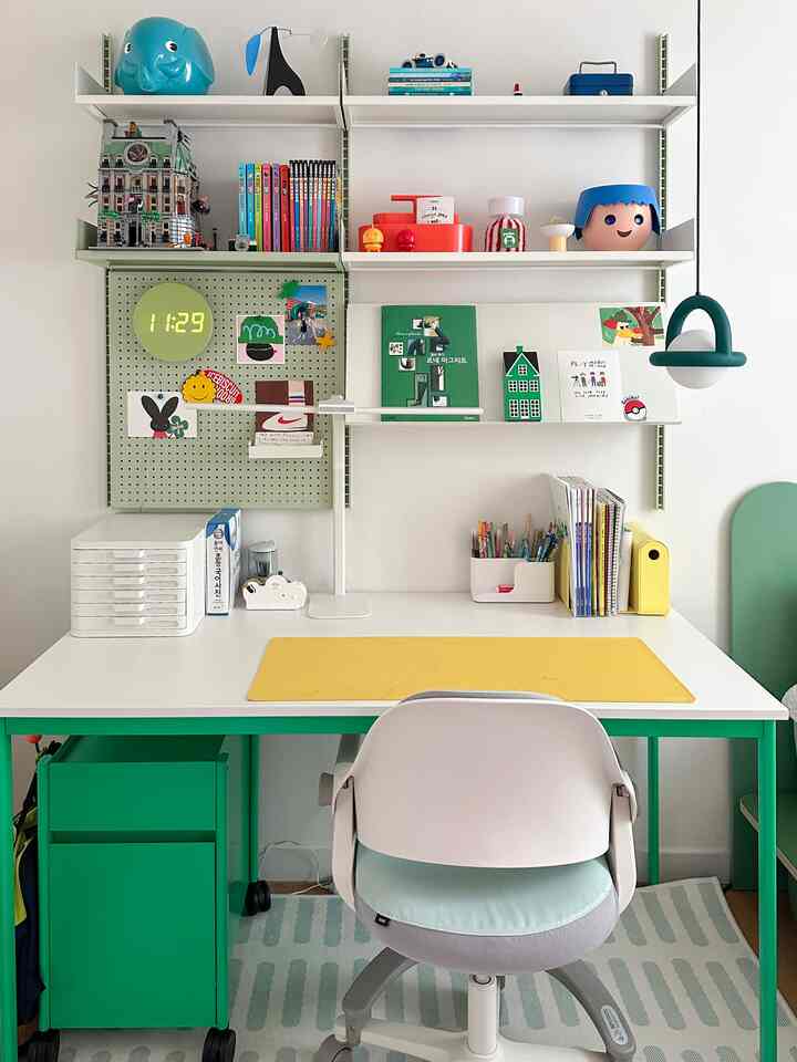 白と緑の色調の子供部屋、子供用デスクと棚、黄色のデスクマットが配置された整った学習空間