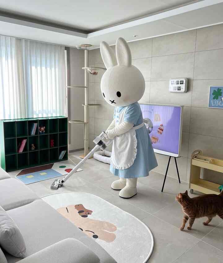 明るくナチュラルな色調のリビング、ソファとキャットタワーが配置され、ミッフィーキャラクターが掃除機をかけている可愛い空間
